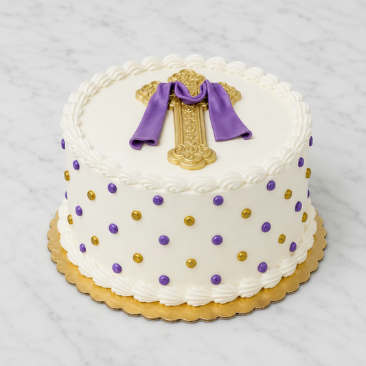 A round white frosted cake with piped scalloped edges, decorated with purple and gold polka dots, topped with a gold ornate cross and purple fondant ribbon,.